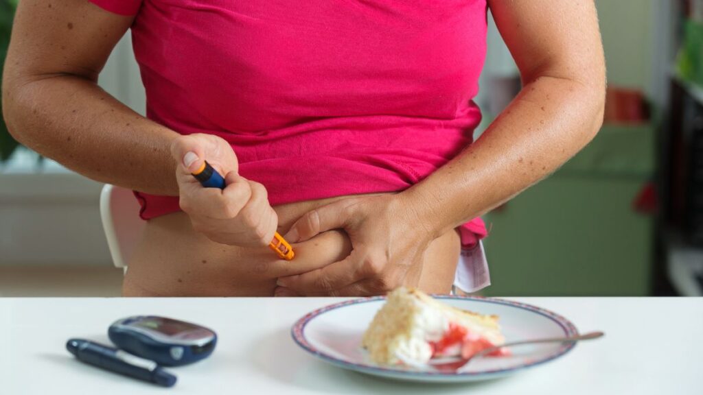 Mulheres têm mais diabetes do que homens? Entenda o que a ciência realmente mostra 1 Mulher aplicando insulina no abdômen com caneta ao lado de medidor de glicose e alimento
