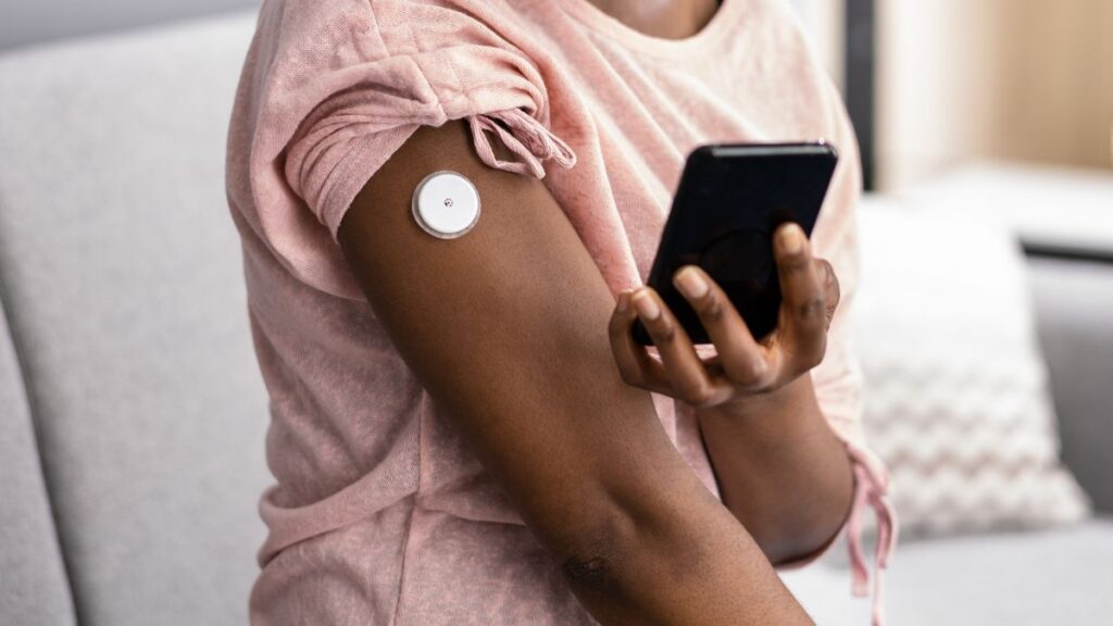 Mulher com sensor de glicose no braço usando celular para monitorar diabetes