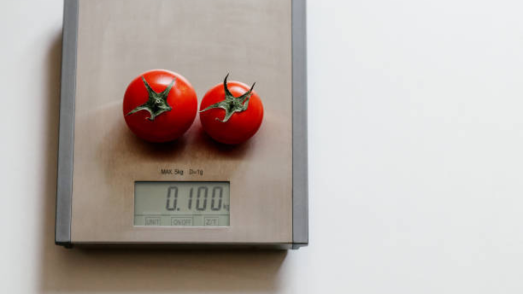 Precisa pesar a comida para controlar a glicemia? Nutricionista explica quando a balança faz sentido Dois tomates vermelhos sobre balança de cozinha