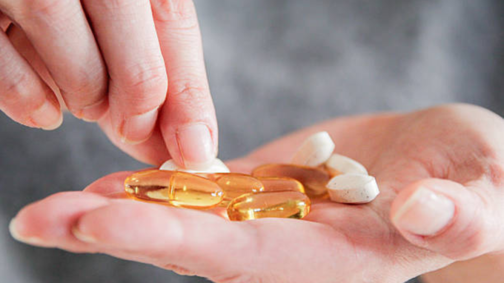 Vitamina D baixa pode afetar quem tem diabetes? Entenda quando a reposição realmente é necessária Mão segurando cápsulas e comprimidos de vitamina D, suplemento relacionado à saúde e diabetes