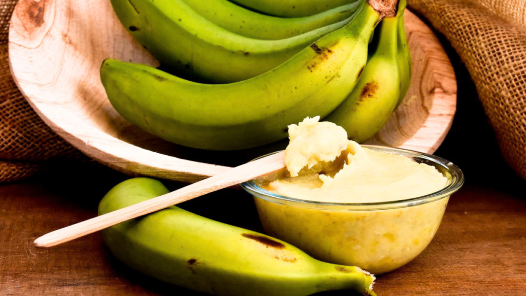 Biomassa de banana verde ajuda a controlar a glicose? Biomassa de banana verde em uma tigela ao lado de bananas verdes sobre uma superfície de madeira.
