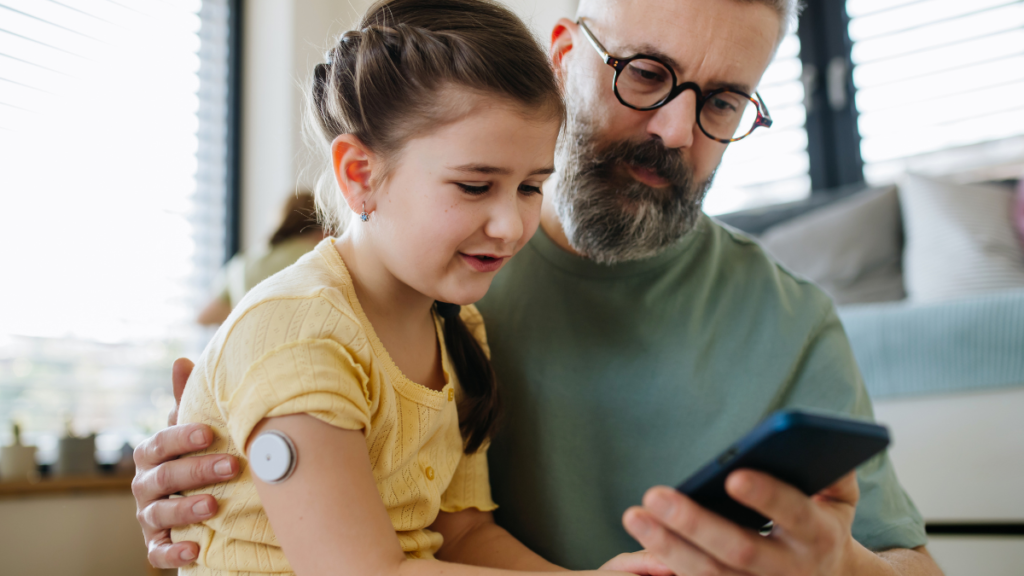 Mais cidades de SP oferecem sensor de glicose pelo SUS; Guaratinguetá entra na lista Menina utiliza sensor de glicose no braço enquanto observa o dispositivo com o pai