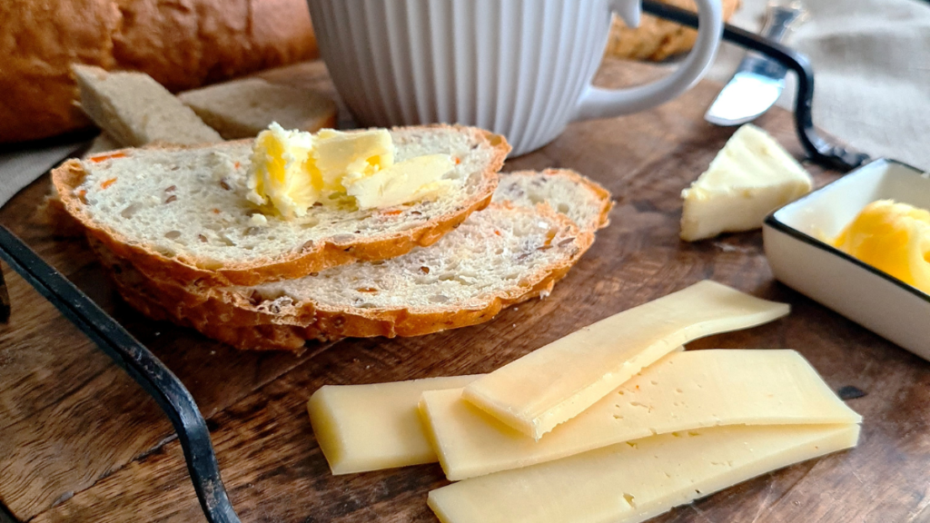 Pão com ovo, queijo ou manteiga muda a glicose? Nutricionista explica Pão fatiado com manteiga e queijo sobre uma mesa de madeira.